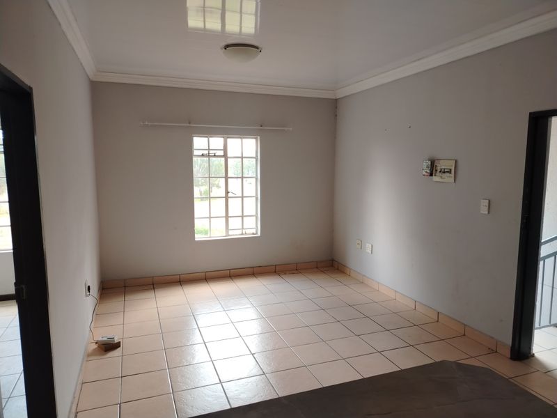 A vacant living area featuring neutral tiled flooring, ceiling cornice, and a window fitted with security burglar bars.