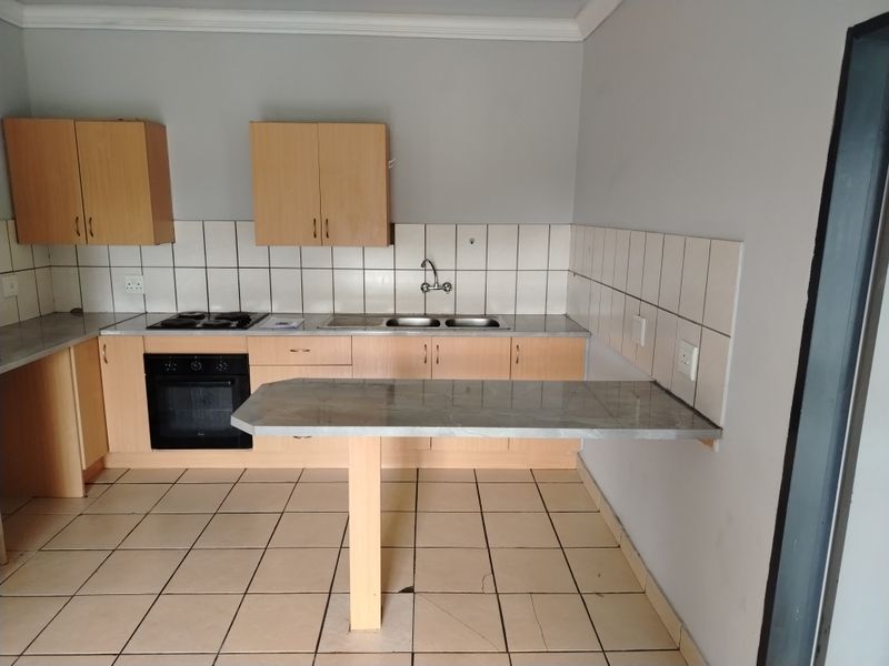 A functional kitchen featuring light wood cabinetry, laminate countertops, a built-in oven and hob, and a convenient breakfast bar extension.