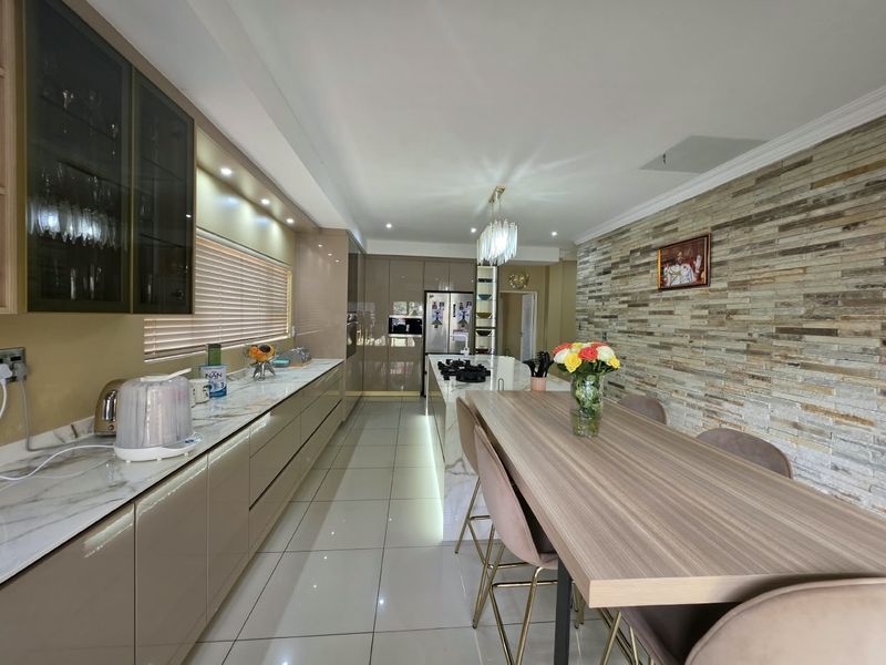 Modern open-plan kitchen and dining area featuring high-gloss cabinetry, marble-look countertops, a stone feature wall, and sleek porcelain floor tiles.