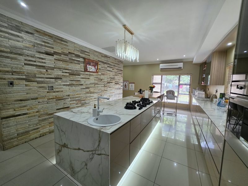 Modern kitchen featuring a large marble-look island with integrated gas hob, stone veneer feature wall, and sleek cabinetry with ambient under-cabinet lighting.