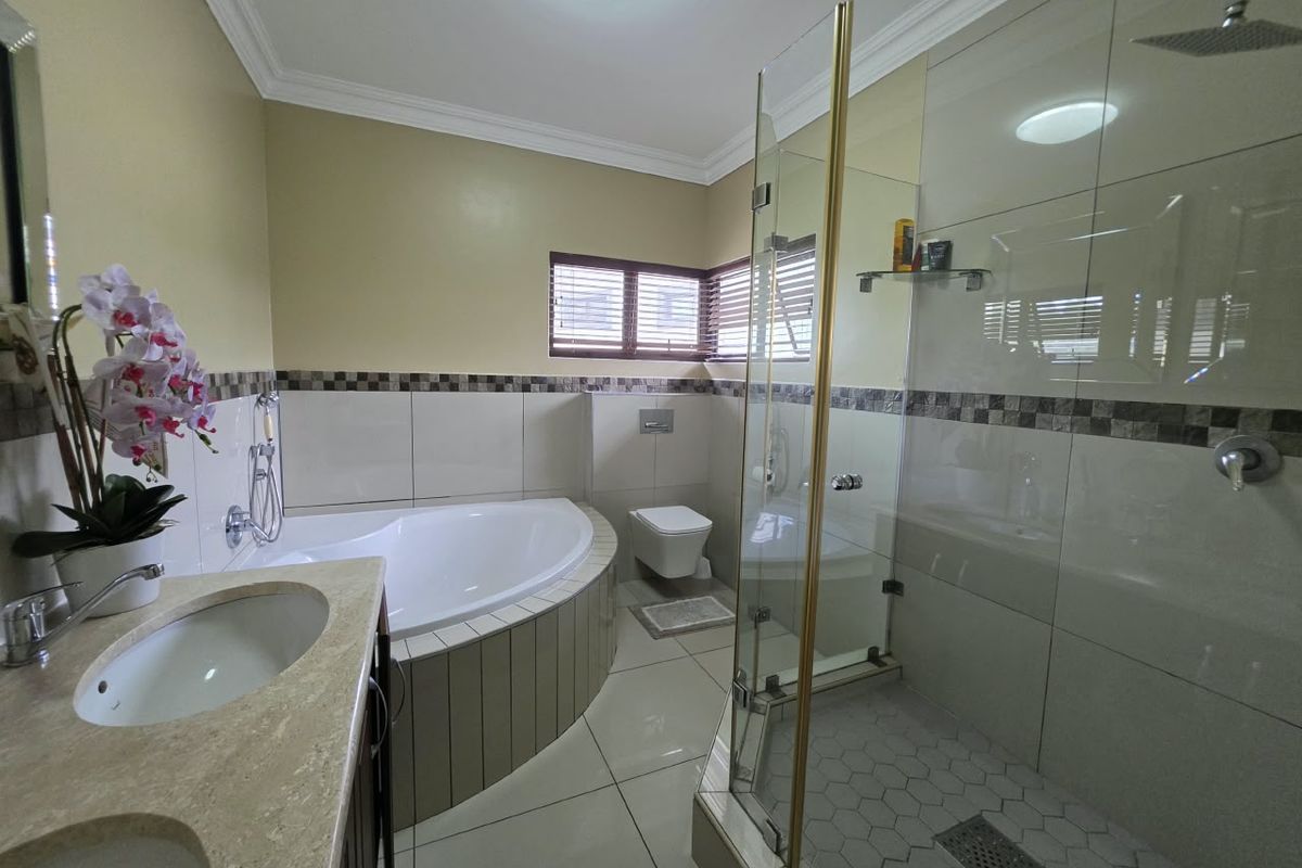 Modern bathroom featuring a corner bathtub, glass-enclosed rain shower, wall-mounted toilet, and a double vanity with stone countertop.