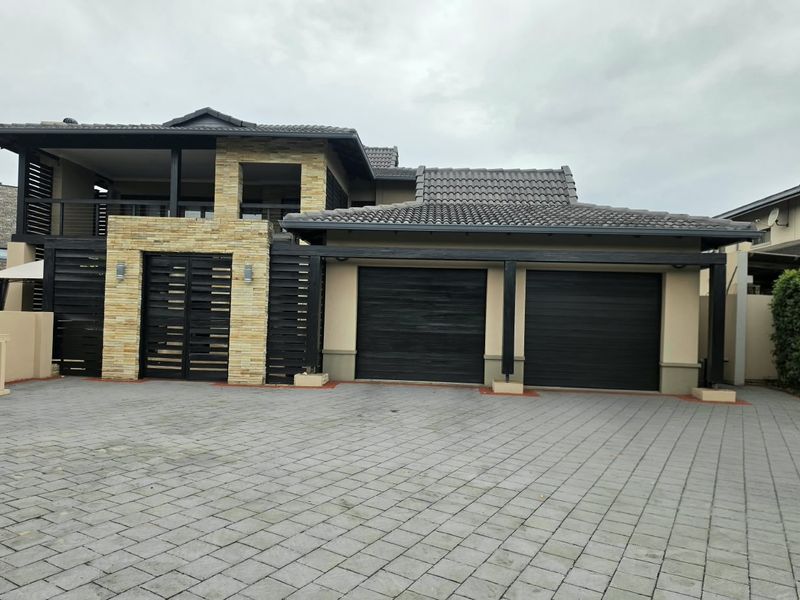 Modern double-storey residence featuring a double garage, stone cladding accents, and a paved driveway with a covered upper-level balcony.