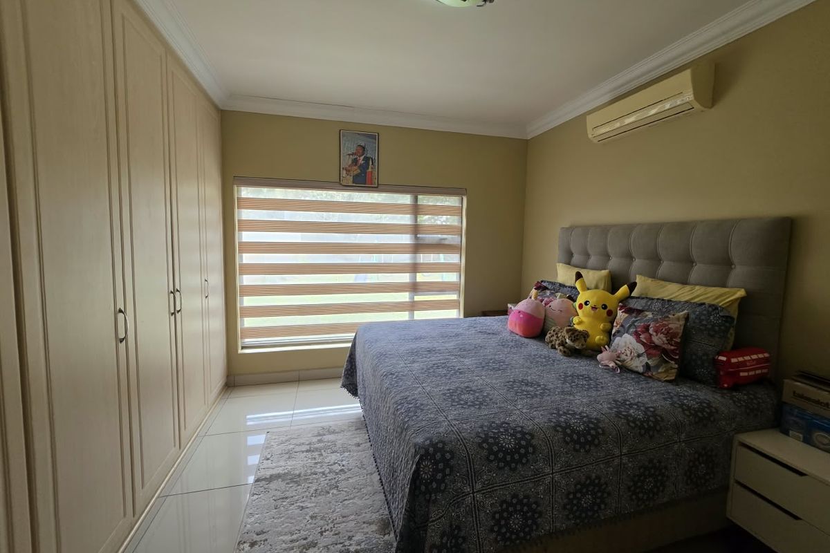 A well-maintained bedroom featuring extensive built-in cupboards, tiled flooring, a split-system air conditioner, and modern zebra blinds.