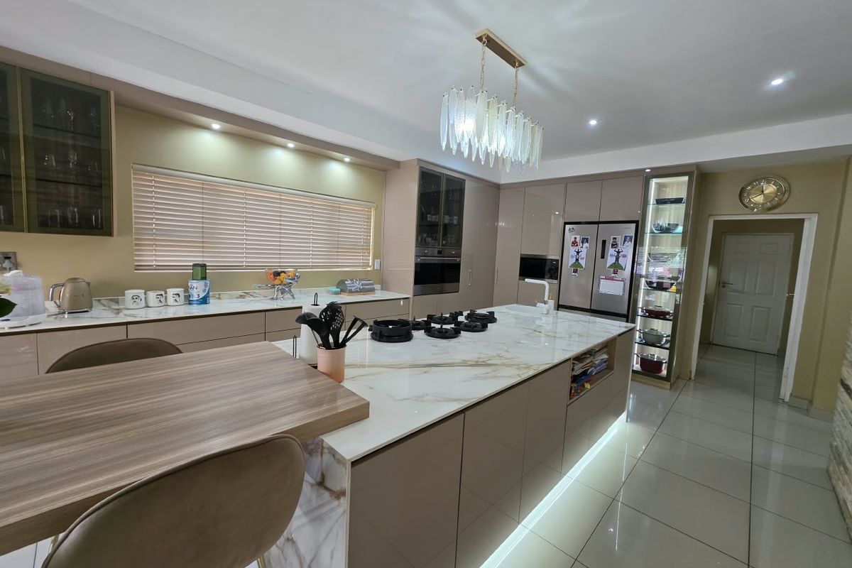 Modern kitchen featuring a large marble-look island with gas hob, integrated appliances, sleek cabinetry, and elegant under-cabinet and plinth lighting.