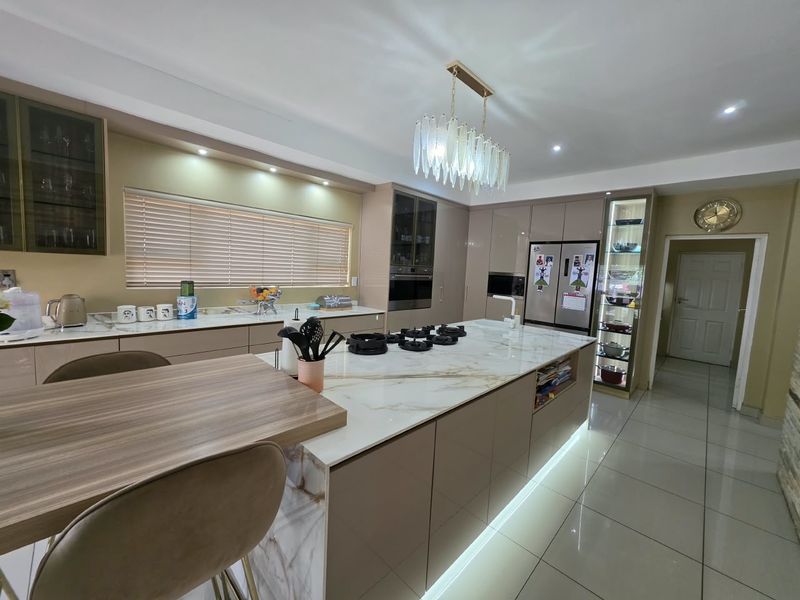 Modern kitchen featuring a large marble-look island with gas hob, integrated appliances, sleek cabinetry, and elegant under-cabinet and plinth lighting.
