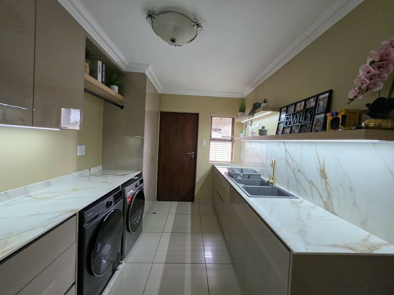 Modern scullery featuring marble-look countertops, gold-finish faucet, double sink, sleek built-in cabinetry, and integrated under-cabinet lighting.