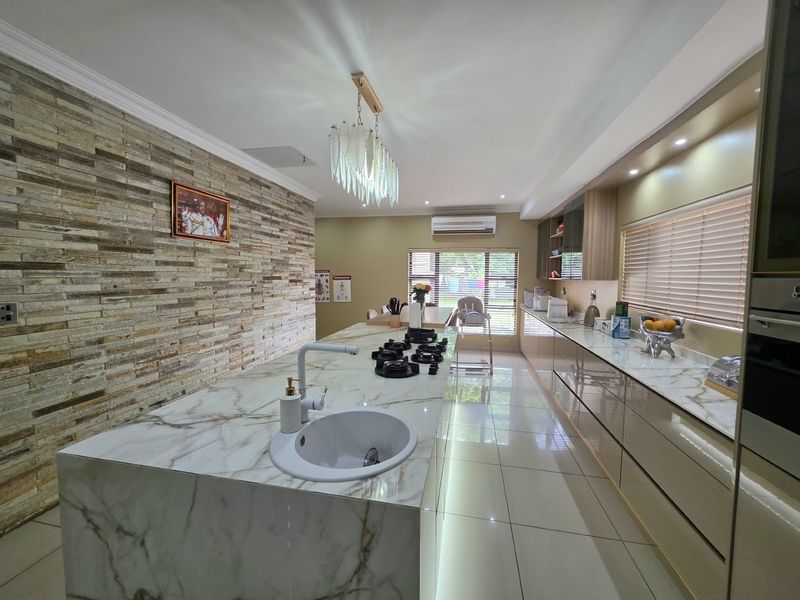 Modern kitchen featuring a large marble-look island with integrated gas hob, high-gloss cabinetry, and a striking stone veneer feature wall.