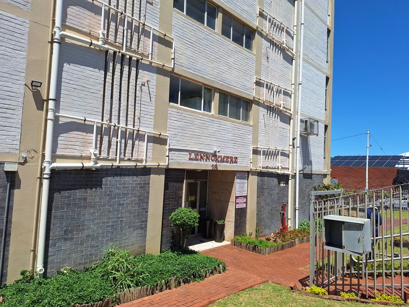 Front entrance view of the Lennoxmere apartment building, featuring a brick facade, paved walkway, and external building infrastructure.