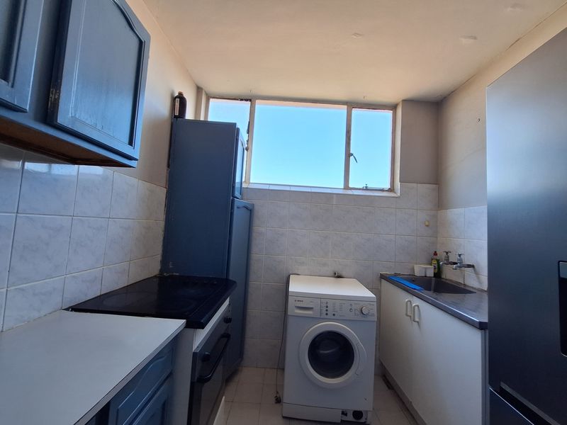 A compact kitchen featuring built-in cabinetry, an electric hob, oven, and a stainless steel sink with tiled splashbacks and flooring.