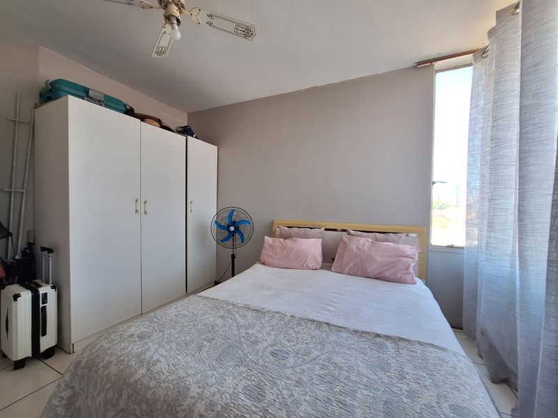 A functional bedroom featuring a built-in wardrobe, ceiling fan, and natural light from a side window.