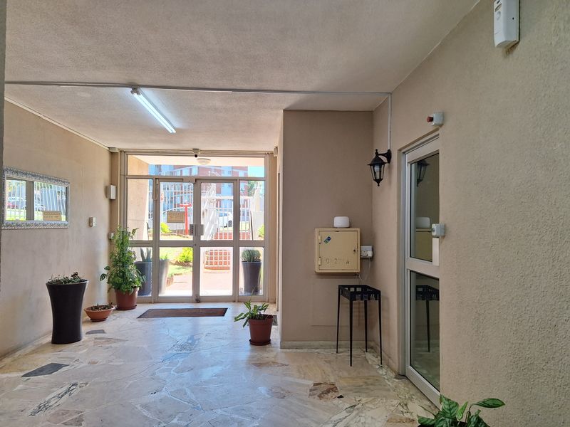 A clean and functional building entrance lobby featuring stone tile flooring, glass panel doors, and secure access points.