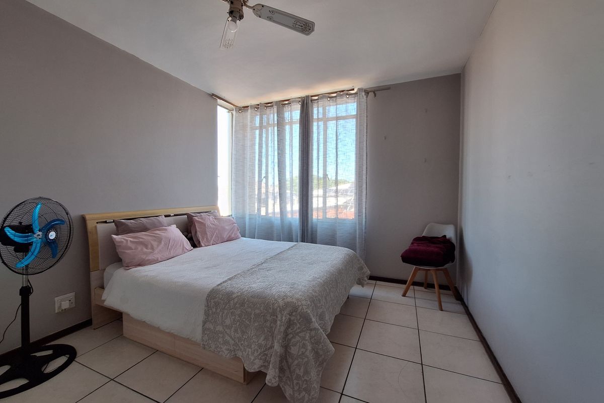 A functional bedroom featuring tiled flooring, a ceiling fan, and large windows with curtain rails, offering a neutral base for personalization.