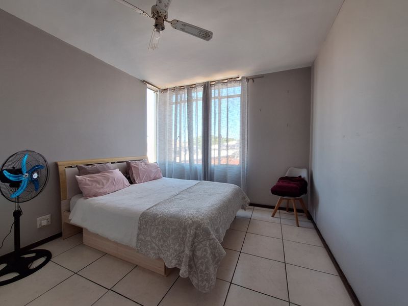 A functional bedroom featuring tiled flooring, a ceiling fan, and large windows with curtain rails, offering a neutral base for personalization.