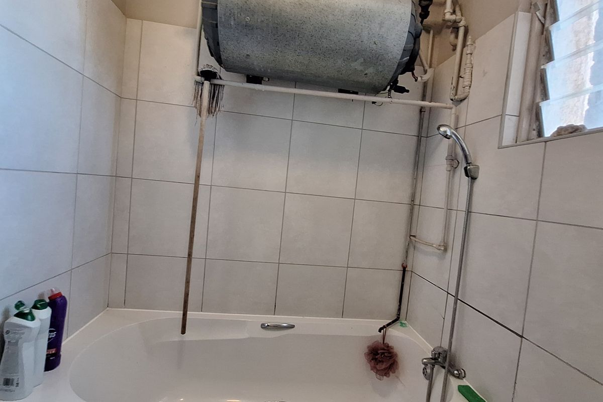 Bathroom featuring a bathtub with shower mixer, tiled walls, and an exposed geyser unit above the bath area.