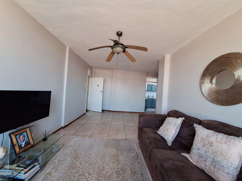 A spacious living area featuring tiled flooring and a ceiling fan, with a clear view through to the kitchen area.