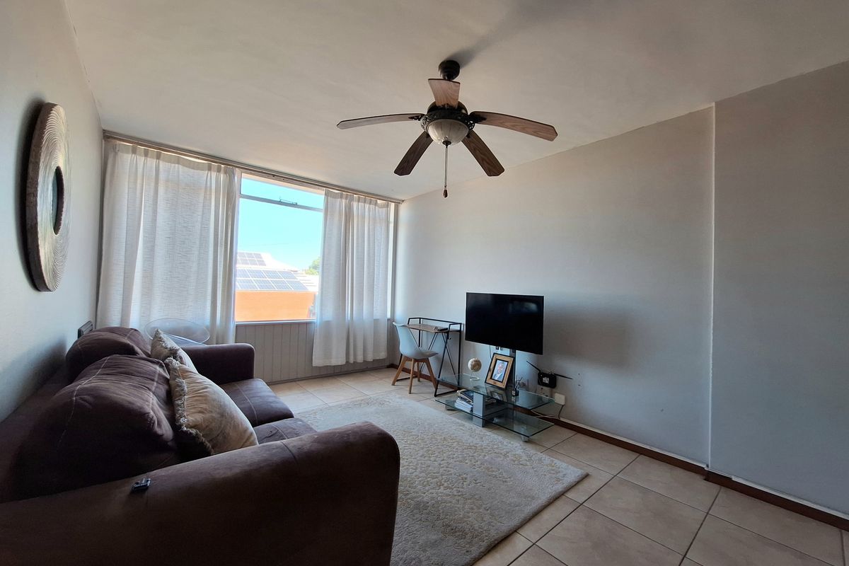 A bright living room featuring tiled flooring, a ceiling fan, and a large window allowing for natural light.