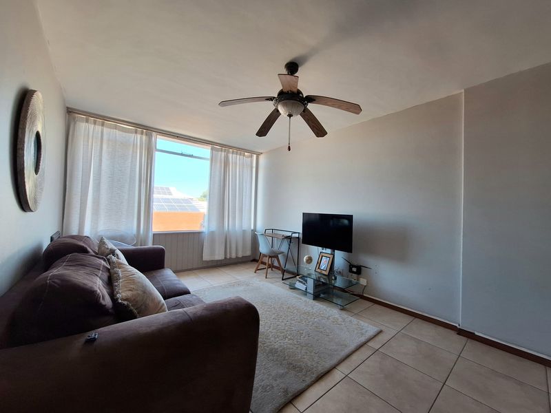 A bright living room featuring tiled flooring, a ceiling fan, and a large window allowing for natural light.