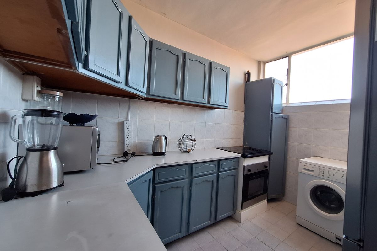 A functional kitchen featuring blue cabinetry, tiled backsplash, built-in oven, hob, and dedicated space for laundry appliances.