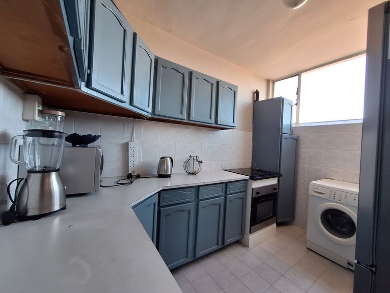 A functional kitchen featuring blue cabinetry, tiled backsplash, built-in oven, hob, and dedicated space for laundry appliances.