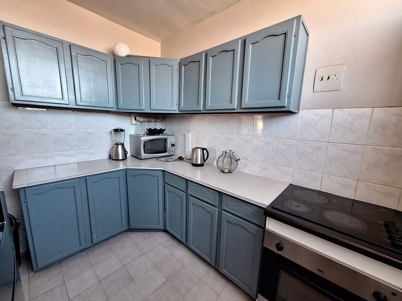 A functional kitchen featuring blue painted cabinetry, a tiled backsplash, and integrated oven and hob, offering a practical layout for daily use.