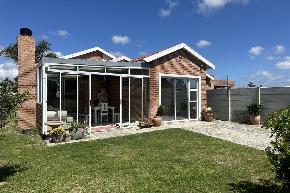 Rear view of a brick house featuring an enclosed patio with sliding glass doors, a paved outdoor area, and a well-maintained garden.