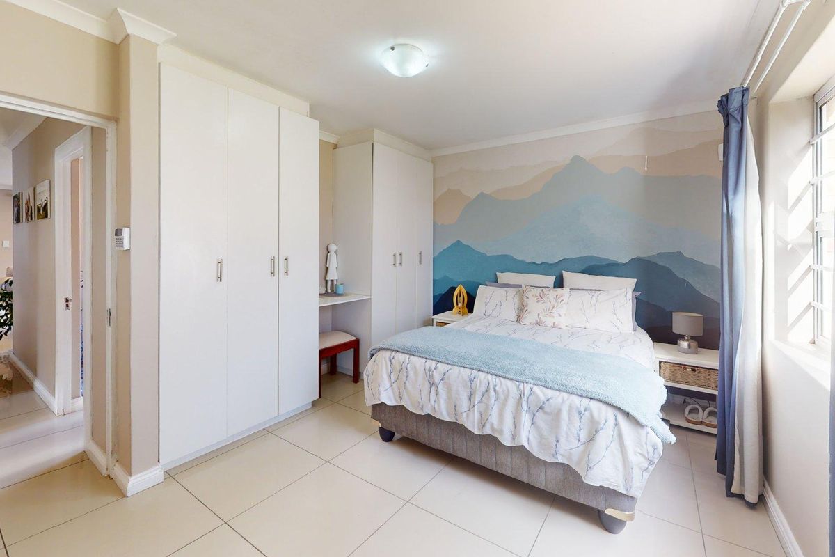 A well-maintained bedroom featuring built-in cupboards, neutral tiled flooring, and a decorative feature wall, offering a clean and functional living space.