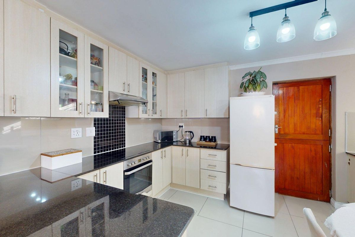 A functional kitchen featuring light-toned cabinetry, dark granite countertops, a built-in oven with extractor fan, and tiled flooring.