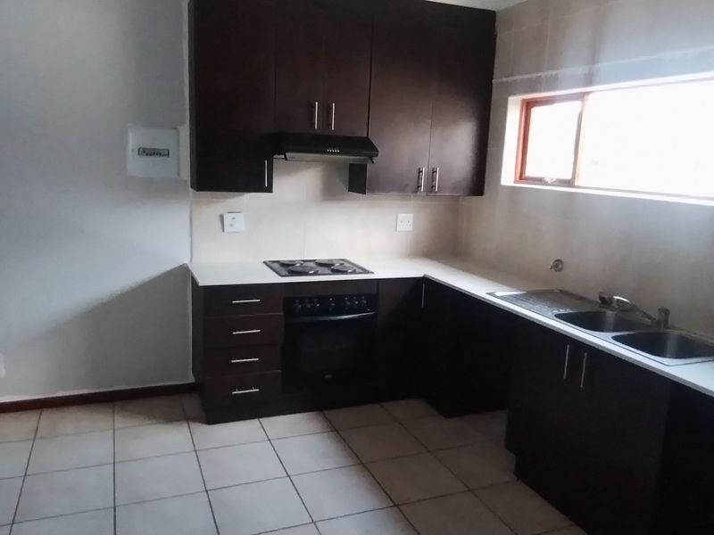 A functional kitchen featuring dark wood cabinetry, built-in oven, electric hob, and double sink with tiled flooring and stone countertops.
