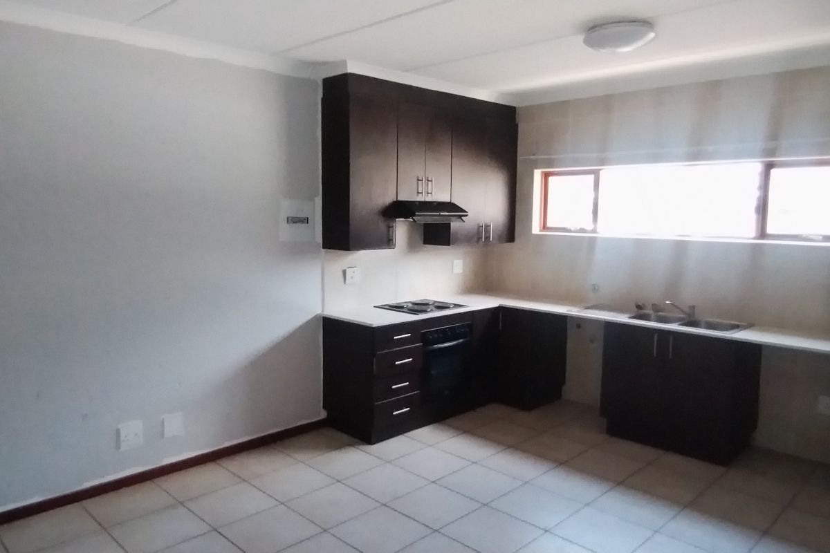 A clean, empty kitchen featuring dark built-in cabinetry, a hob, oven, extractor fan, and a double sink with tiled flooring.