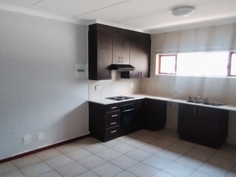 A clean, empty kitchen featuring dark built-in cabinetry, a hob, oven, extractor fan, and a double sink with tiled flooring.