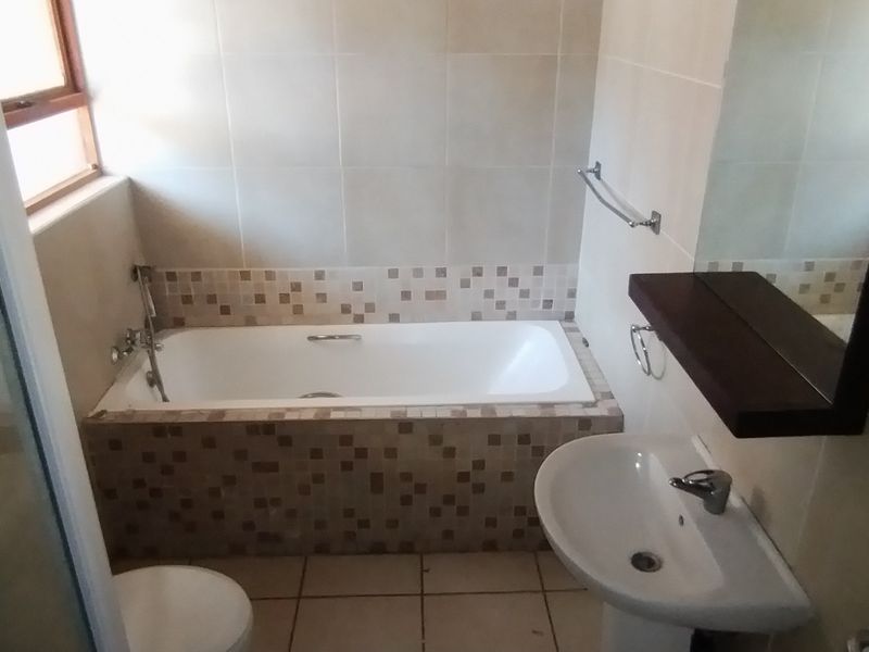 A functional bathroom featuring a built-in bathtub with mosaic tile detailing, a pedestal basin, and a separate shower enclosure.