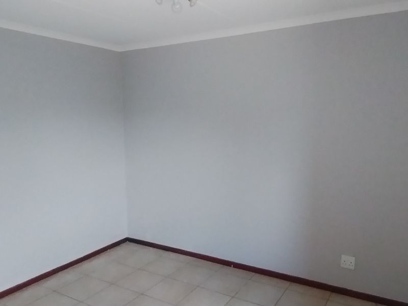 A clean, empty bedroom featuring neutral grey walls, tiled flooring, and dark skirting boards, providing a blank canvas for personalization.