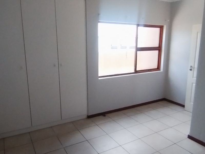 A bright, empty bedroom featuring neutral tiled flooring, built-in cupboards, and a window with an aluminium frame.
