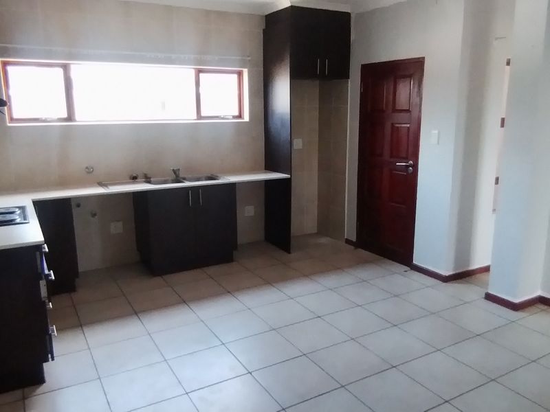 An empty kitchen featuring dark built-in cabinetry, light countertops, a double sink, an electric hob, and tiled flooring.