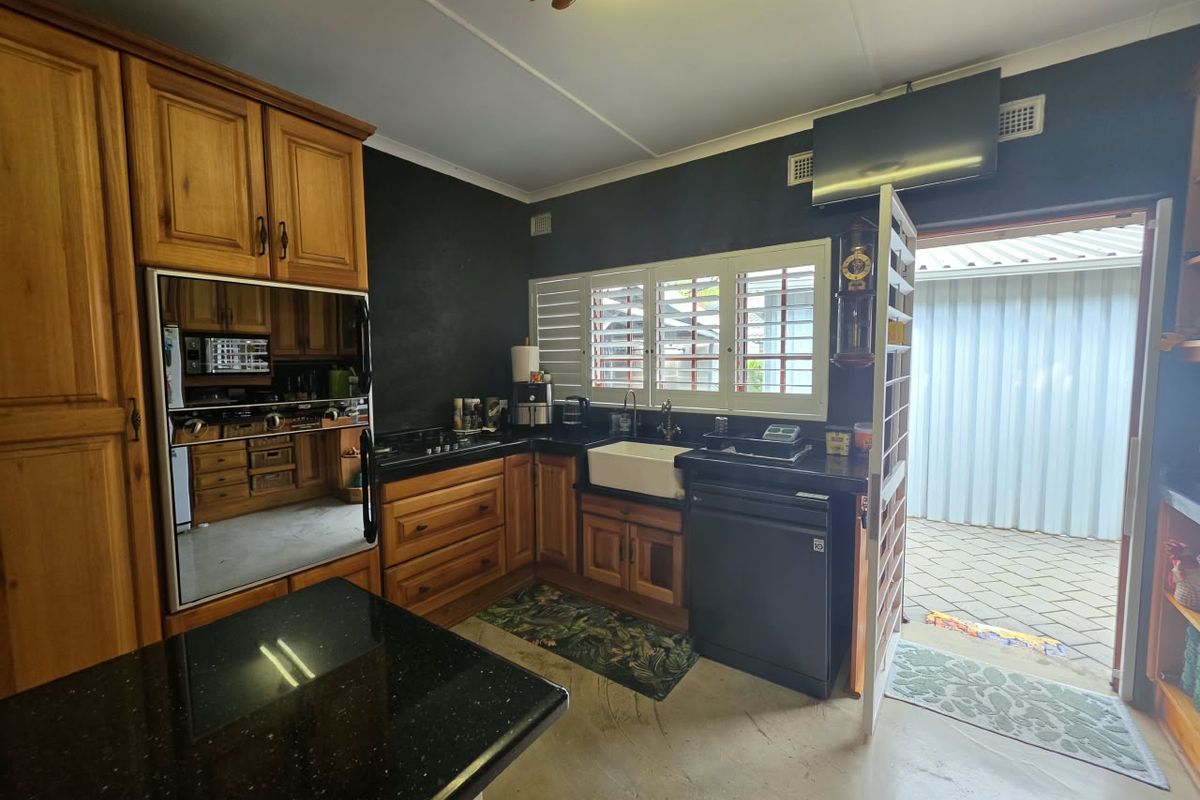 A functional kitchen featuring warm wooden cabinetry, contrasting black granite countertops, a farmhouse sink, and direct access to an outdoor paved area.