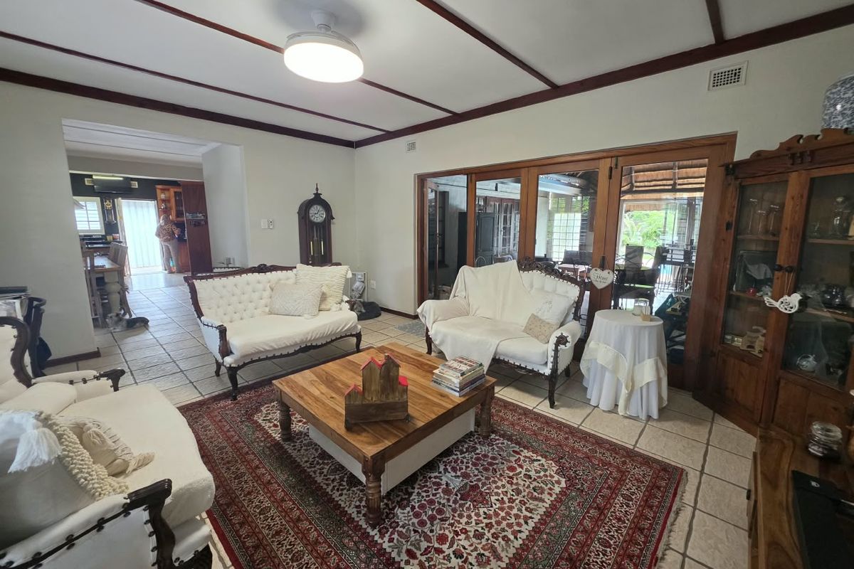 Spacious living room featuring exposed timber ceiling beams, tiled flooring, and large timber-framed sliding doors providing access to the outdoor patio area.