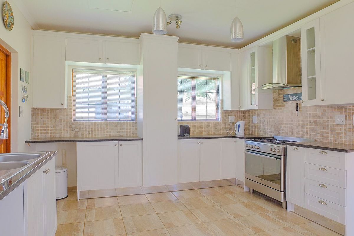 A well-maintained kitchen featuring white cabinetry, granite countertops, a stainless steel gas stove with extractor fan, and a tiled backsplash.