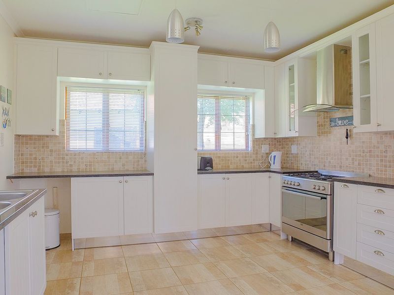 A well-maintained kitchen featuring white cabinetry, granite countertops, a stainless steel gas stove with extractor fan, and a tiled backsplash.