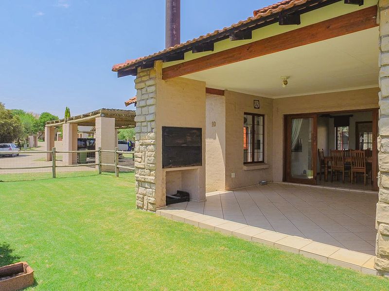 Covered patio area featuring a built-in braai, tiled flooring, and stone-clad pillars, providing seamless access to the garden.