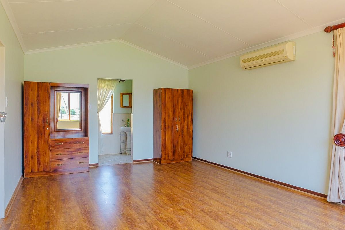 Spacious bedroom featuring laminate flooring, a vaulted ceiling, and a wall-mounted split-system air conditioner, with direct access to an en-suite bathroom.