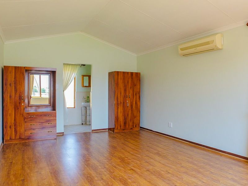 Spacious bedroom featuring laminate flooring, a vaulted ceiling, and a wall-mounted split-system air conditioner, with direct access to an en-suite bathroom.