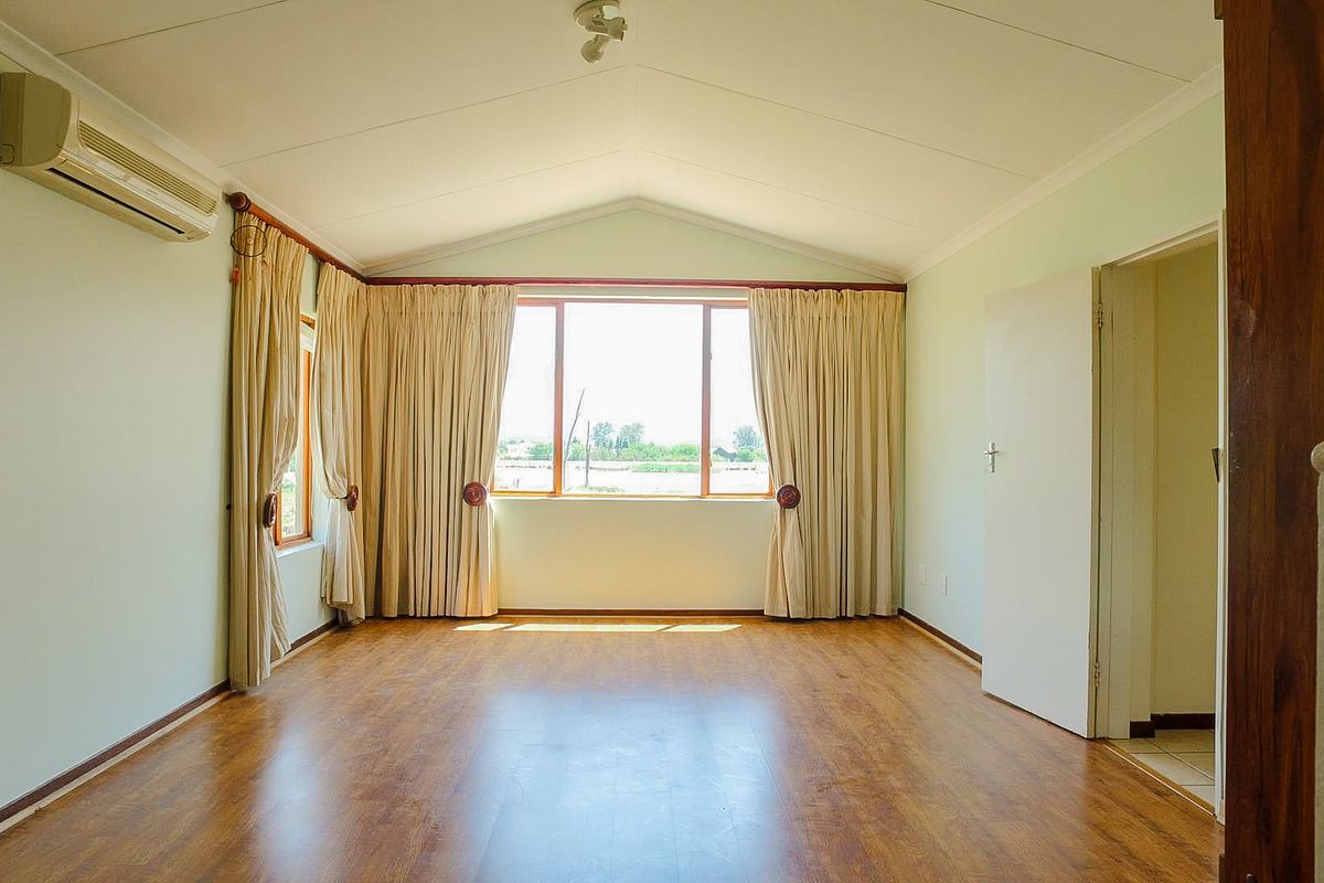 Spacious living room featuring vaulted ceilings, laminate flooring, and a wall-mounted air conditioning unit, offering a bright and open atmosphere.