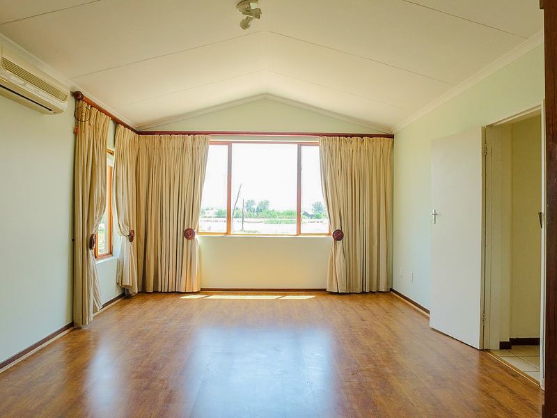 Spacious living room featuring vaulted ceilings, laminate flooring, and a wall-mounted air conditioning unit, offering a bright and open atmosphere.