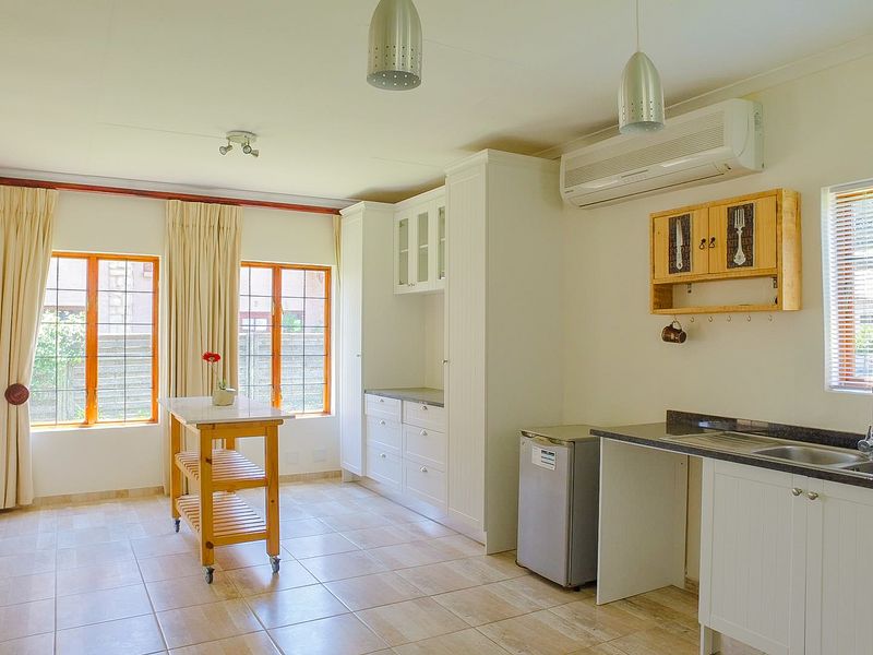 A bright kitchen featuring white cabinetry, granite countertops, double sink, and split-system air conditioning, with tiled flooring and natural light.