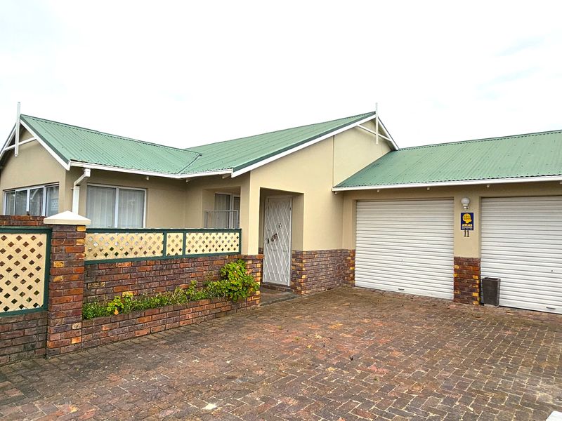 Front elevation of a townhouse featuring a double garage, brick paved driveway, and a low brick boundary wall with lattice detailing.