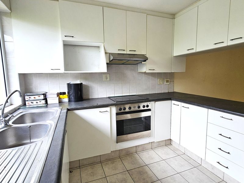 A functional kitchen featuring white cabinetry, dark laminate countertops, a built-in oven with hob, and a double sink with tiled backsplash.