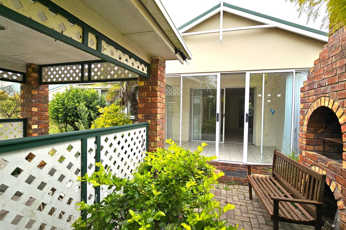 A covered patio area featuring a built-in brick braai, lattice screening, and sliding glass doors leading into the interior living space.