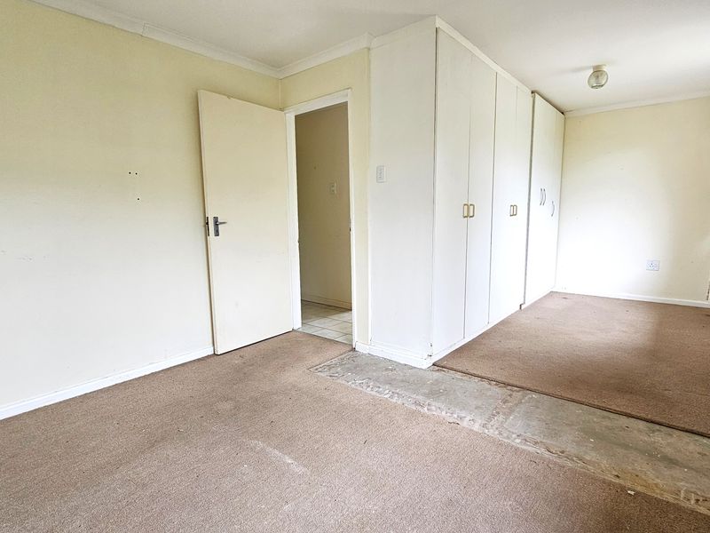 An empty bedroom featuring built-in cupboards, coving, and carpet flooring that requires replacement due to visible wear and exposed subfloor sections.