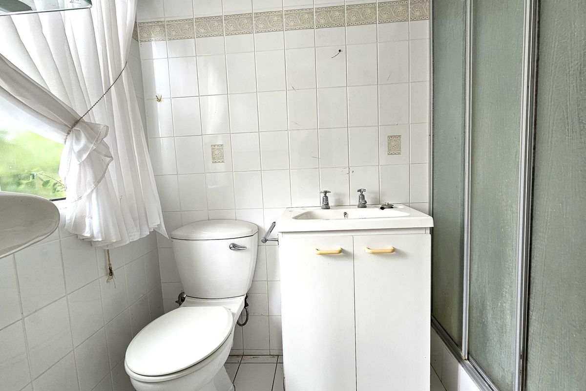 A dated bathroom featuring a vanity cabinet, toilet, and shower enclosure with white wall tiling throughout.