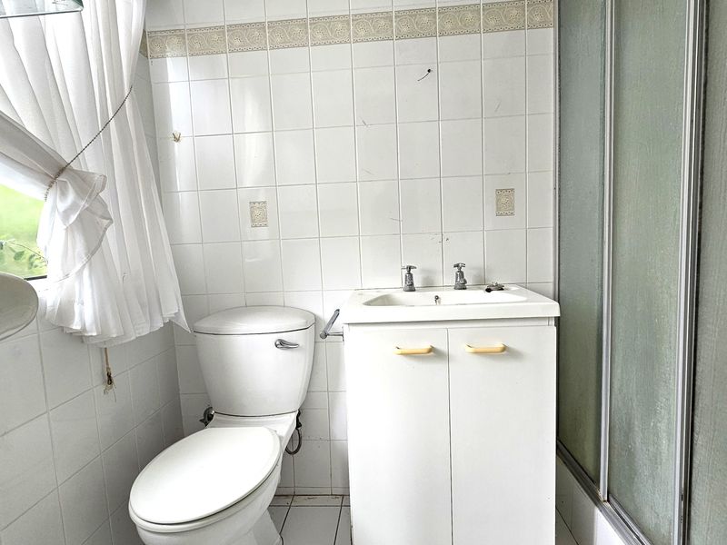 A dated bathroom featuring a vanity cabinet, toilet, and shower enclosure with white wall tiling throughout.